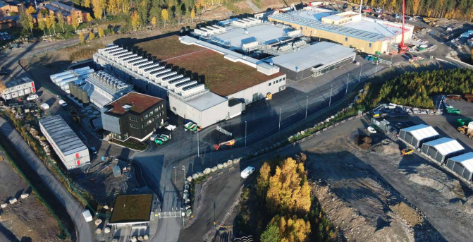 Flygfoto över EcoDataCenters campus med flera byggnader och träd på hösten. Flygfoto över EcoDataCenters campus med flera byggnader och träd på hösten.